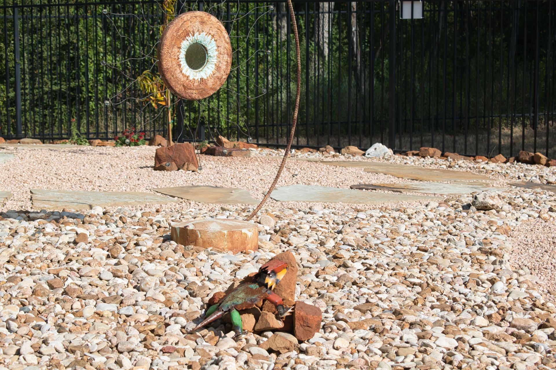 Outdoor sculpture garden with circular metal art and a lizard sculpture on pebbles.