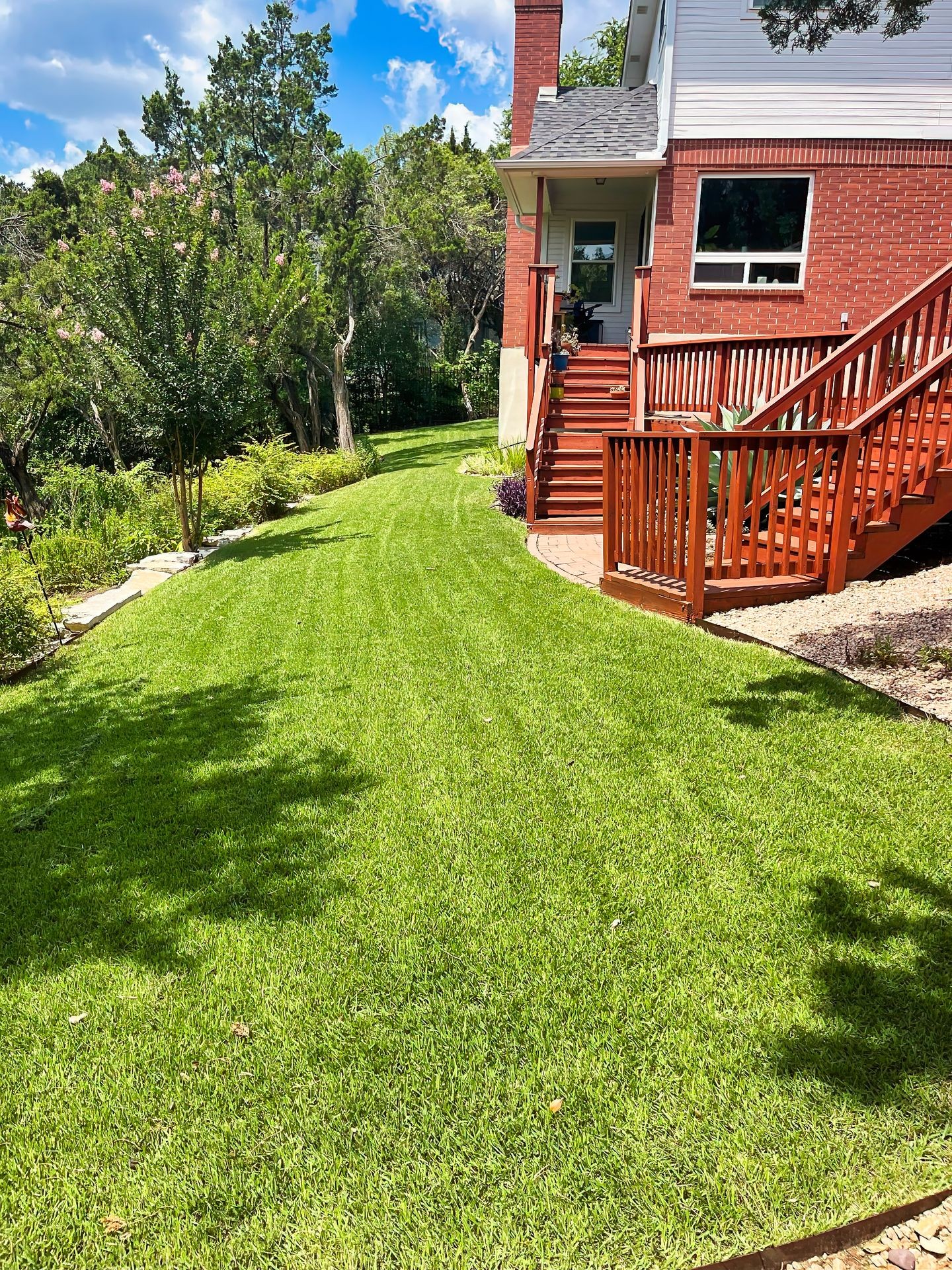 Well-manicured lawn with a wooden deck and stairs leading up to a house