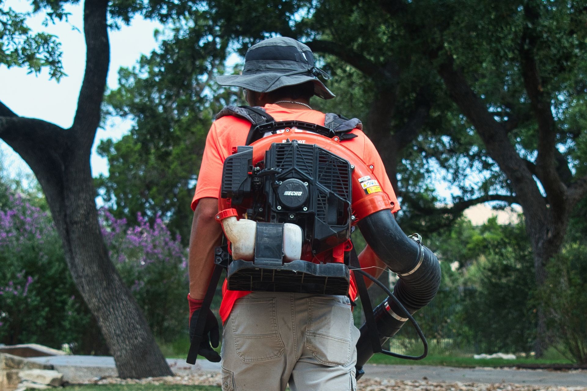 Person using a backpack leaf blower in a park, surrounded by trees.